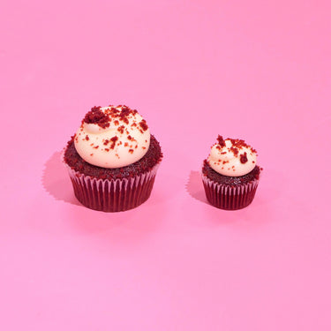 Red Velvet Cupcakes by Crumbs & Doilies with cream cheese icing and red velvet crumbs on pink background.
